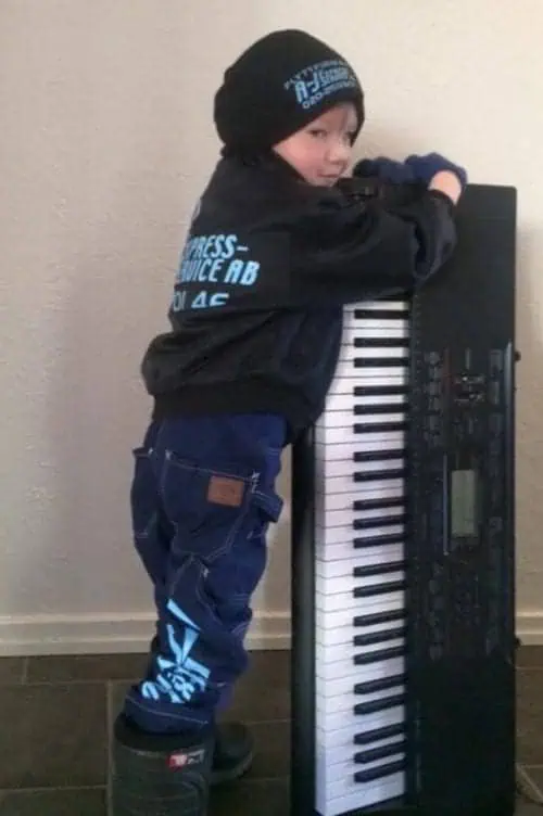 Barn som leker med ett keyboard, klädd i mössa och jacka.