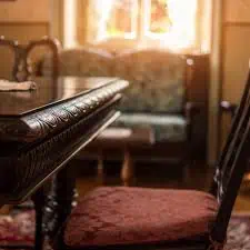 Bild av ett gammalt, tomt vardagsrum med antika möbler och en solig fönsterutsikt.